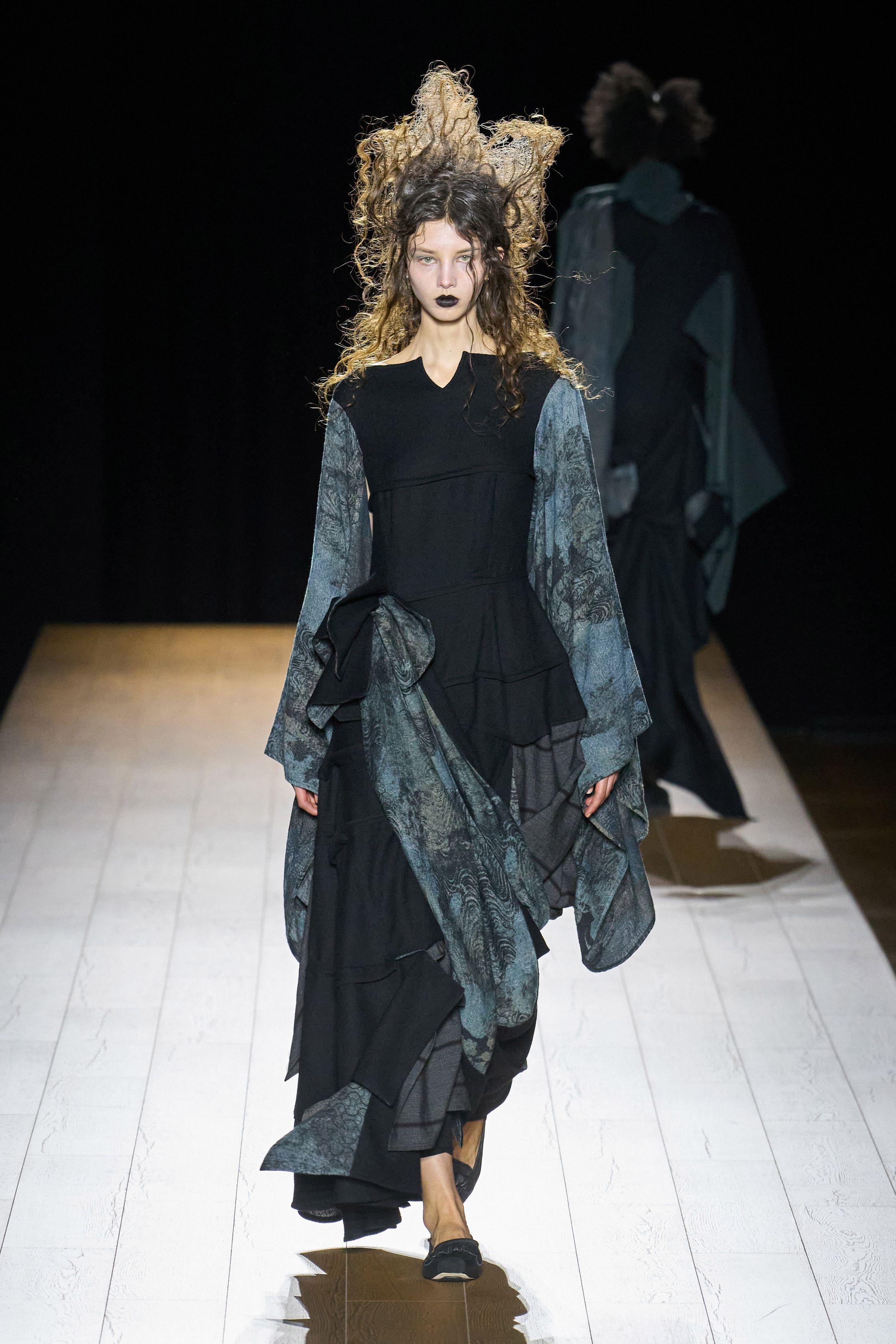 Yohji Yamamoto 本季依然延续标志性的黑色哲学：宽松层叠轮廓、和服式结构与手工拼接面料形成一种诗意而深沉的东方美学。夸张头饰与飘逸衣摆让整场秀像一场黑色戏剧，既神秘又极具艺术感-顽石频道趋势研究